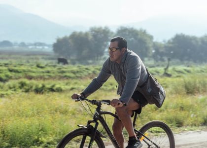 Adult man cycling on a rural path in a natural landscape, wearing casual attire.