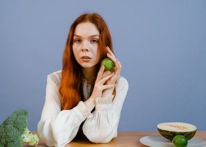 Woman with red hair holding lime surrounded by fresh produce on table.